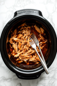 This image shows chicken being shredded directly in the crockpot using two forks