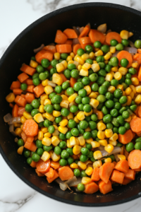 this image shows A vibrant mix of peas and corn being added to the creamy sauce in the pot, enhancing the vegan chickpea pot pie pasta with a pop of color and sweetness.