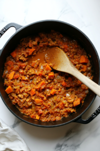 This image shows diced sweet potatoes and a blend of spices being added to a soup pot, building the rich and flavorful base for the vegan sweet potato soup.