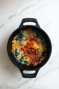 this image shows Tomato paste, red chili flakes, and dried oregano sizzling in a pot of heated oil, forming the aromatic and spicy base for the creamy tomato pasta sauce.