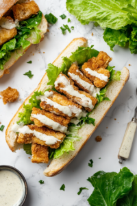 The final step of layering crispy chickpea patties, fresh lettuce, and vegan Caesar dressing on a toasted bun to create a perfect sandwich.