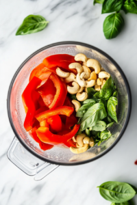 this image shows A blender filled with roasted red peppers, cashews, and spices, being blended into a smooth, creamy sauce for the Roasted Red Pepper Cashew Cream Pasta.