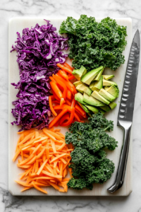 this image shows An array of vibrant vegetables, including carrots, red peppers, and cucumbers, being sliced and prepped for the Vegan Rainbow Peanut Noodles.