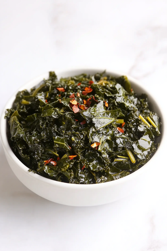 This image presents a flavorful bowl of kale, slow-cooked and garnished with red chili flakes for extra flavor.
