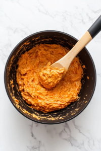 this image shows dollop of vegan cream cheese being stirred into the simmering pasta sauce, adding creaminess to the one-pot tomato pasta