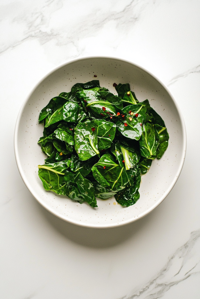This image showcases a plate of tender slow-cooked collard greens, garnished with red chili flakes for a spicy kick.