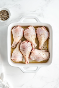 This image shows raw chicken drumsticks being coated with a blend of spices, ensuring rich flavor before baking.