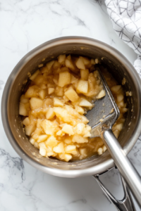 This image shows cooked apples being mashed into a smooth, thick applesauce with a fork or masher, achieving the perfect texture.