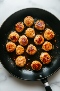 This image shows perfectly browned meatballs being carefully arranged in a slow cooker, ready to soak up flavor.