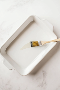 This image shows a baking dish being greased with butter or oil, preventing the shells from sticking during baking.