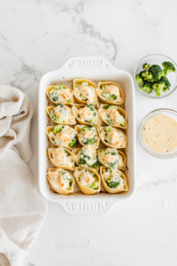 This image shows stuffed pasta shells being arranged in a baking dish, ready for the Alfredo sauce and cheese topping.