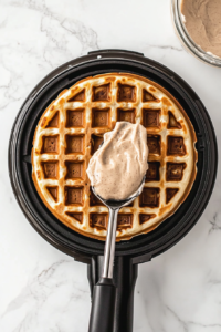 This image shows a ladle pouring thick waffle batter onto the hot waffle iron, ensuring an even spread for a perfectly cooked waffle.