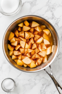 This image shows chopped apples, cinnamon, and other ingredients being combined in a pot, ready to be simmered into a flavorful applesauce.
