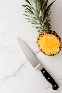 This image shows a pineapple being carefully cut in half, with the interior being prepared to hold rice and chicken for the teriyaki pineapple bowl.