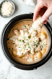 This image shows shredded mozzarella and Parmesan cheese being generously sprinkled over the cooked chicken and potatoes, ready to melt into the creamy sauce.