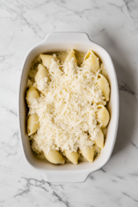 this image shows topping the stuffed Shells with cheese to create an extra cheesy layer over the dish after baking adding extra flavor to the dish