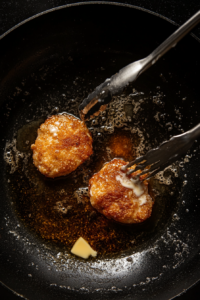 This image shows a chicken breast being flipped in the pan, revealing a crispy golden-brown crust as it cooks on the other side.