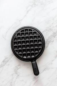 This image shows a waffle iron heating up on the countertop, ready to cook fresh homemade waffles to golden perfection.