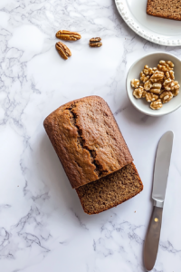 This image shows a loaf of banana bread freshly sliced on a wooden cutting board, revealing its moist texture. A butter knife rests nearby, ready for serving.