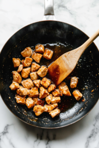 This image shows golden-brown chicken pieces being coated in a thick, glossy teriyaki sauce, ensuring every bite is packed with rich, savory flavor.