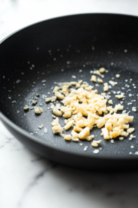 This image shows finely chopped ginger and garlic sizzling in a hot pan, releasing their fragrant aromas as the base for the sauce.