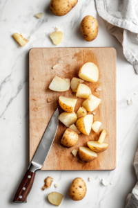 This image shows freshly peeled and quartered potatoes on a cutting board, prepared for cooking. Properly cutting them ensures even cooking and crispiness.