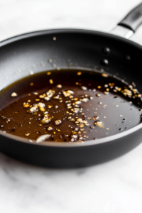 This image shows finely chopped ginger and garlic sizzling in a hot pan, releasing their fragrant aromas as the base for the sauce.