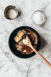 This image shows a saucepan filled with a glossy blend of butter, cocoa powder, sugar, and milk as it begins to melt together. The deep chocolate color hints at the rich, fudgy flavor these no-bake cookies will have.
