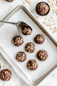 This image shows cookie dough being scooped onto parchment paper using a spoon, forming soft and round mounds. The mixture holds its shape while still appearing rich, fudgy, and slightly glossy.