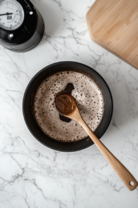 This image shows a saucepan with the chocolate mixture actively bubbling, indicating that it has reached the perfect rolling boil stage. This crucial step ensures the cookies will set properly once mixed with the oats.