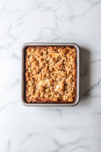 This image shows smooth vanilla icing being drizzled over the slightly warm cinnamon crumble coffee cake right before serving.