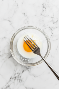 This image shows egg and milk being whisked together in a mixing bowl, creating a smooth and well-combined mixture for the Parkin cake batter.