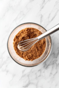 This image shows a mixing bowl filled with flour, cinnamon, brown sugar, and white sugar, combined with melted butter until the texture resembles wet sand.
