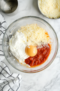 This image shows a creamy cheese sauce being whisked together in a saucepan with parmesan, milk, and butter.