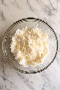 This image shows a top-down view of a glass bowl with creamy butter and coconut extract on a white marble countertop.