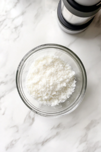 This image shows a top-down view of a glass bowl with cake mix, water, eggs, oil, and coconut extract ready to be mixed, on a white marble countertop.