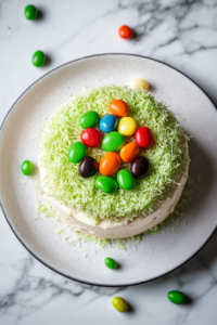 This image shows a top-down view of the finished cake with green coconut scattered on top and jelly beans placed in the center on a white marble countertop.