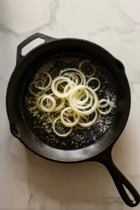 adding-onions-to-black-skillet-white-marble-background-clean-scene