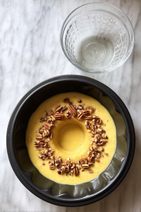 cake-batter-poured-into-black-bundt-pan-over-pecans-on-white-marble